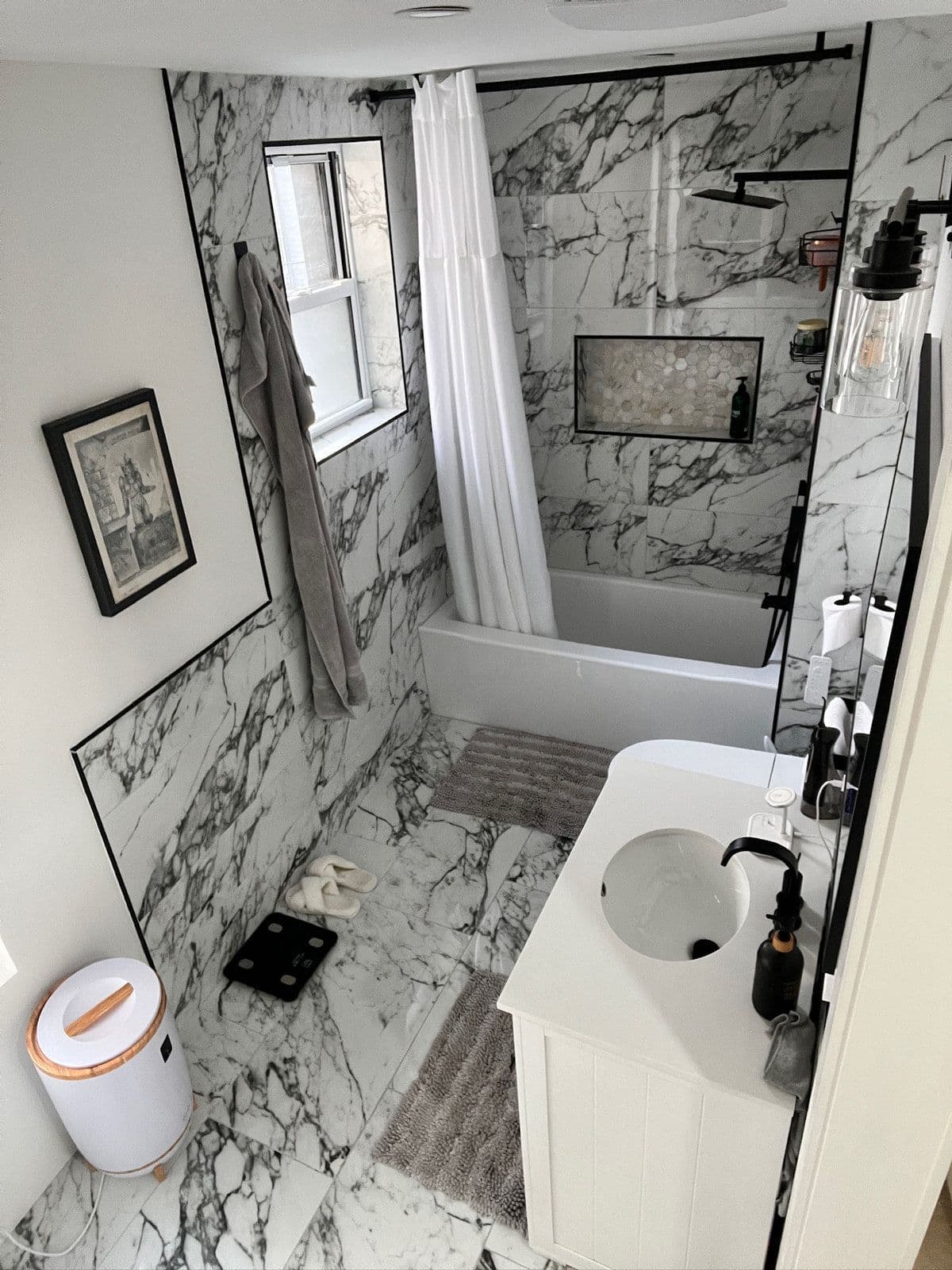 The same bathroom finished in large-format marble tile, with a new tub, black fittings, a glass shower screen and a framed print on the wall.