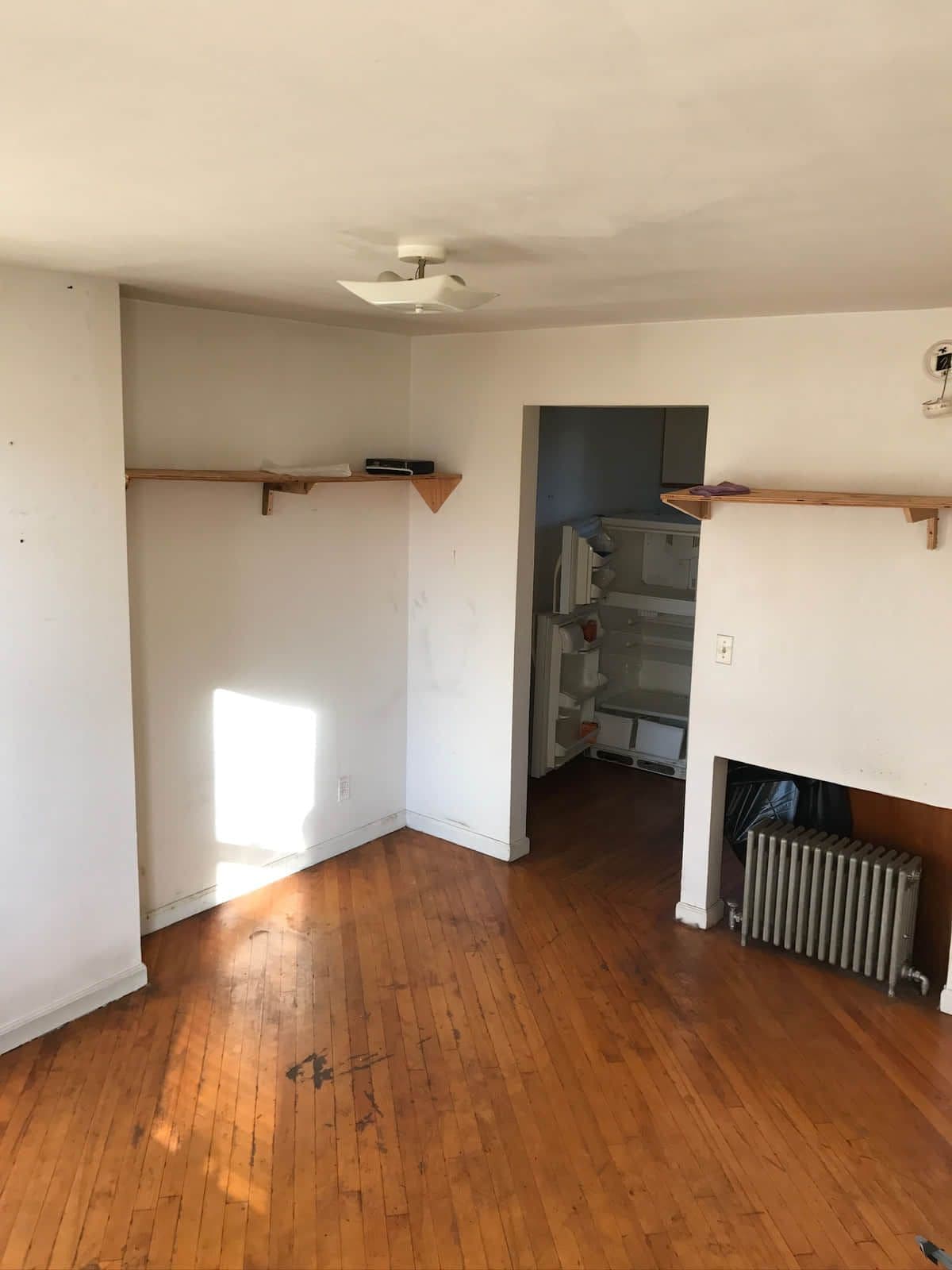An empty bedroom before work started: bare hardwood boards, a picture rail, an exposed radiator and a doorway through to the hall.