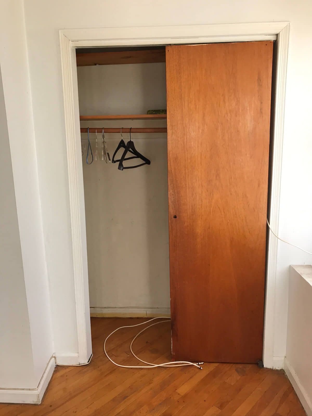 A bedroom closet closed off by two sliding wooden doors, with worn hardwood floor and a loose cable running along the skirting.