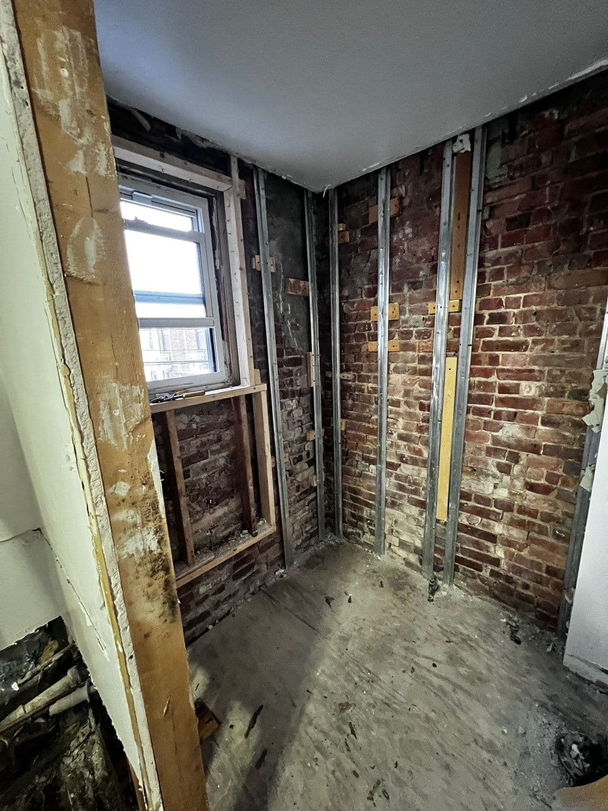 The party wall taken back to the original brick, with steel studs set out ready for new drywall around the window.