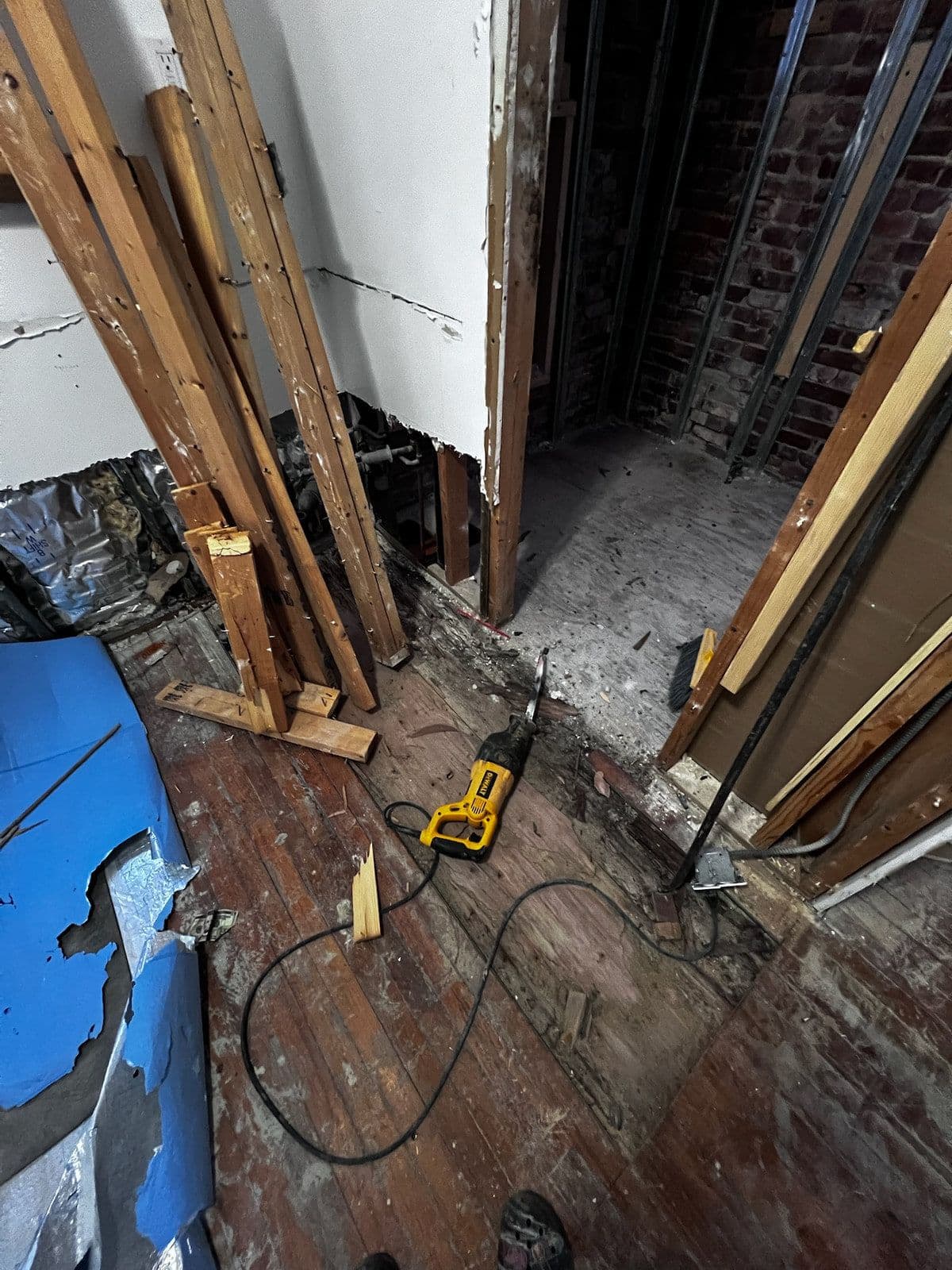 New timber studs stood up against the exposed floor joists, with the old subfloor lifted and insulation board stacked to one side.