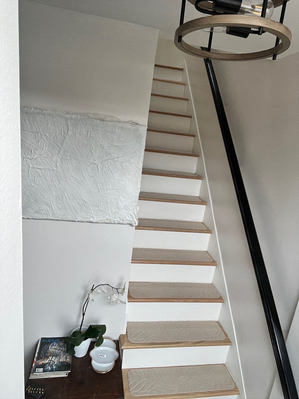 The rebuilt staircase: white risers, new treads with a runner, a black railing and a ring light overhead.