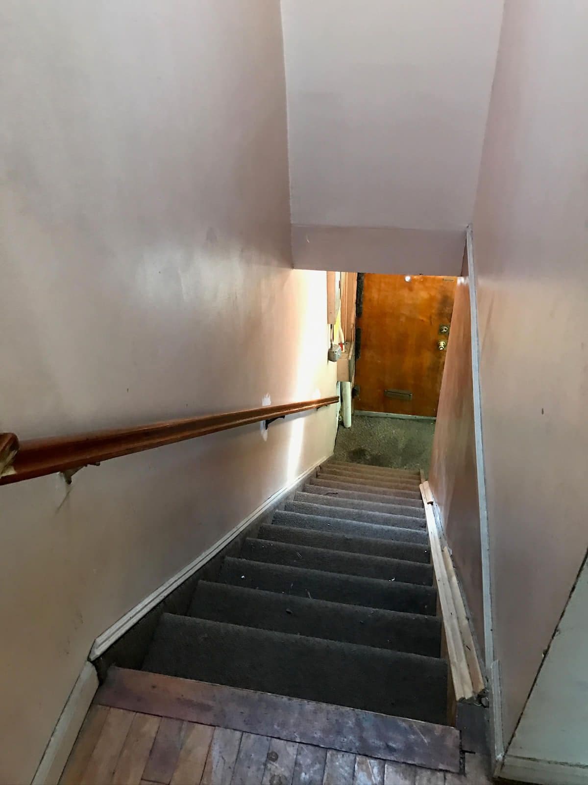 The original staircase seen from the top — worn dark carpet on the treads, a copper handrail and scuffed plaster.