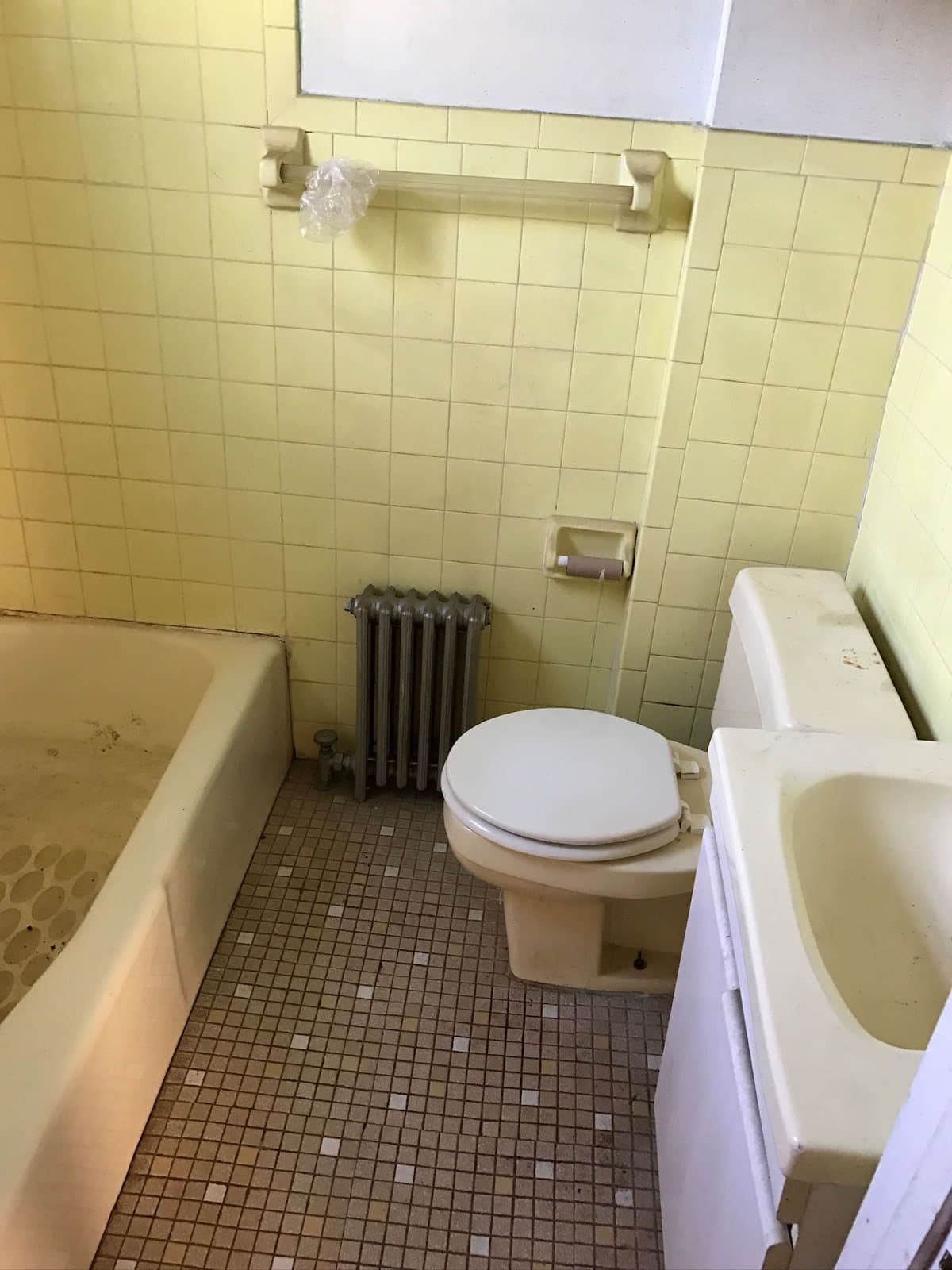 The old bathroom looking toward the basin — yellow tile, a brown mosaic floor, an exposed radiator and a wall-hung sink.