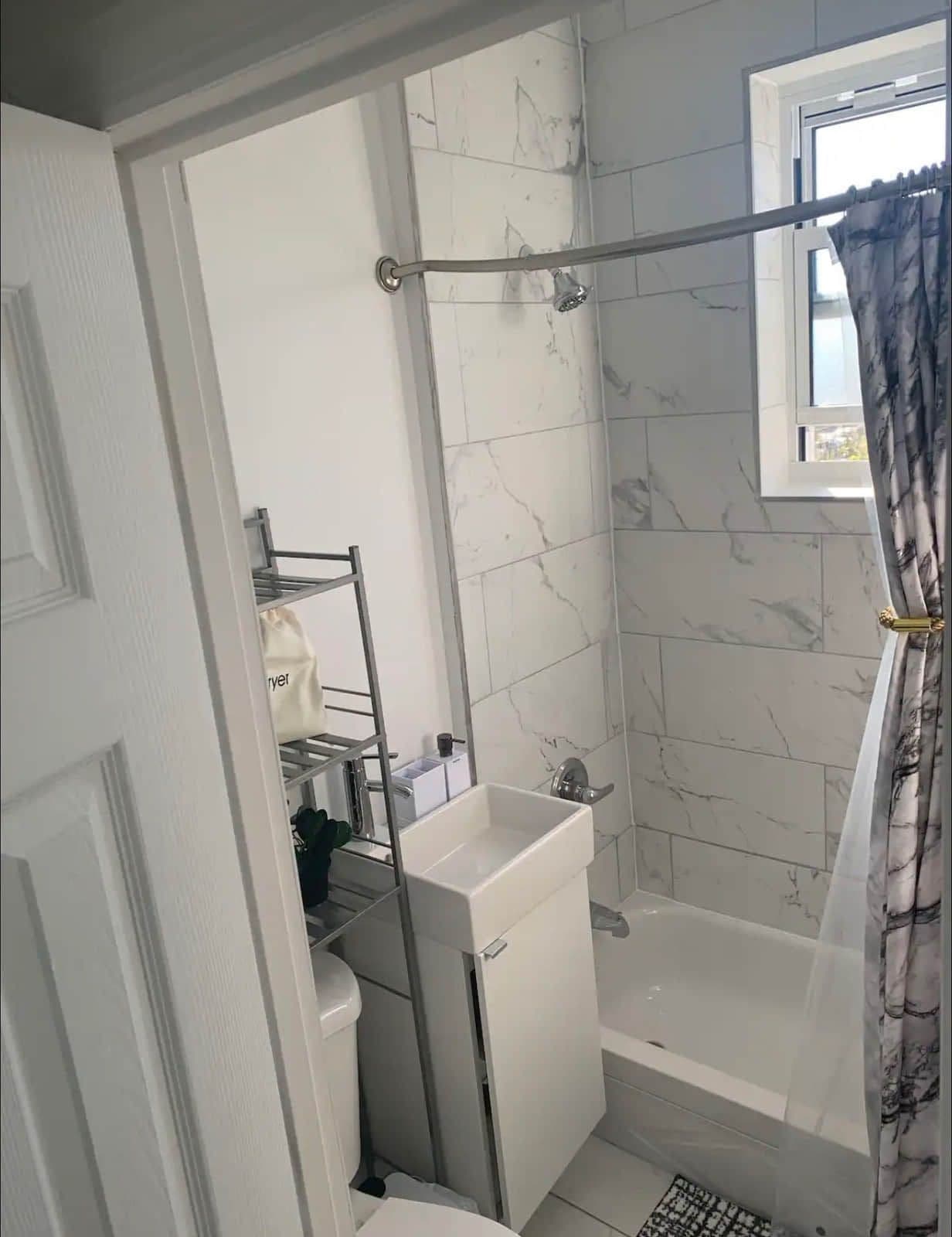 The compact bathroom: marble-effect tile, a new tub and shower, and a wall-hung basin over a small cabinet.