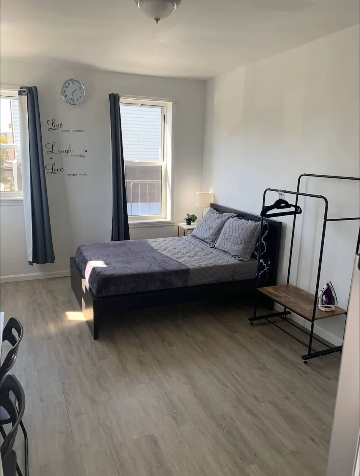 The sleeping area: a made bed under two windows, floor-length curtains and a freestanding clothes rail.