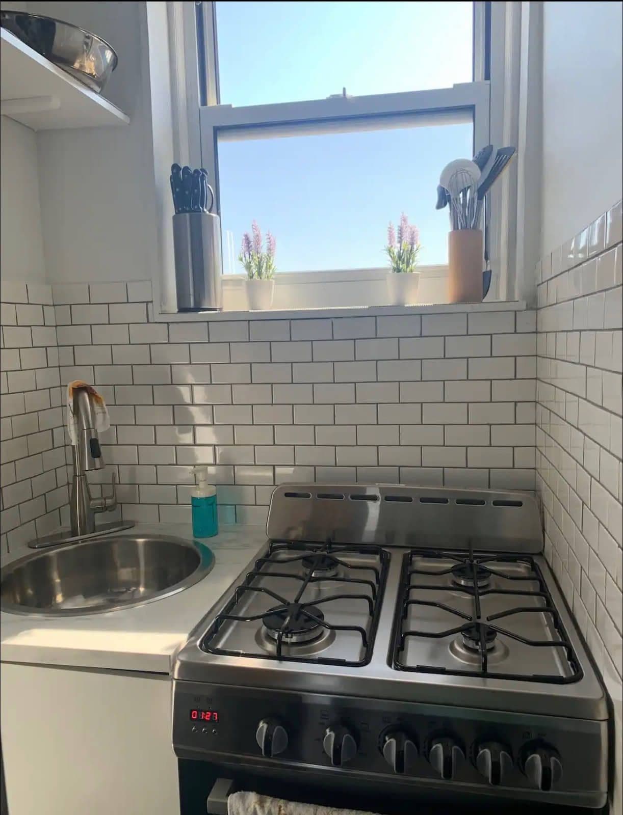 The counter and stainless sink under the window, tiled to the ceiling.