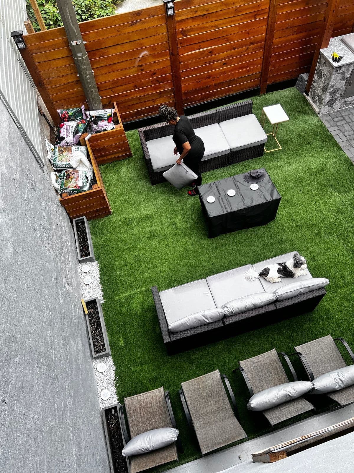 The finished yard seen from above: a lawn, a cedar fence, built-in timber planters, outdoor sofas and loungers, and a stone-clad counter in the corner.