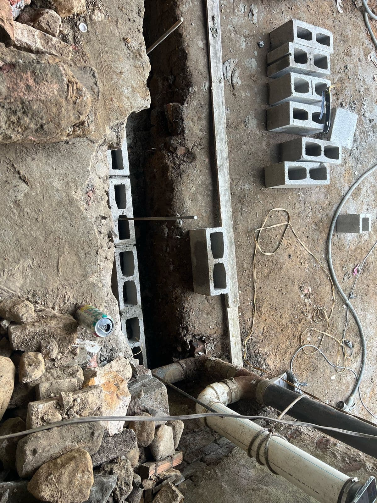New drainage and waste pipework run along the old stone foundation, with blocks set out ready to build back over it.