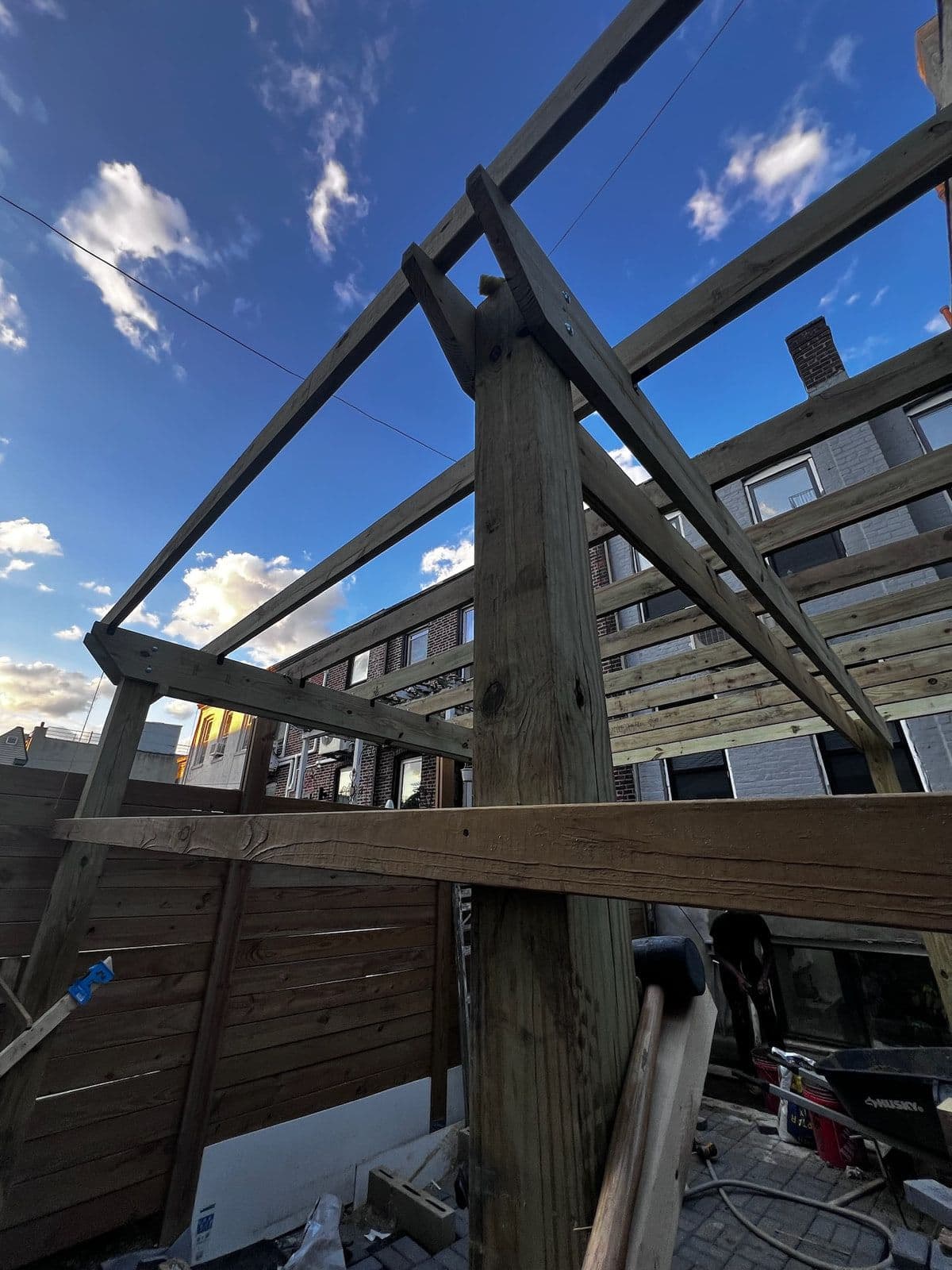 The pergola frame standing against the sky, seen from underneath before the roof went on.