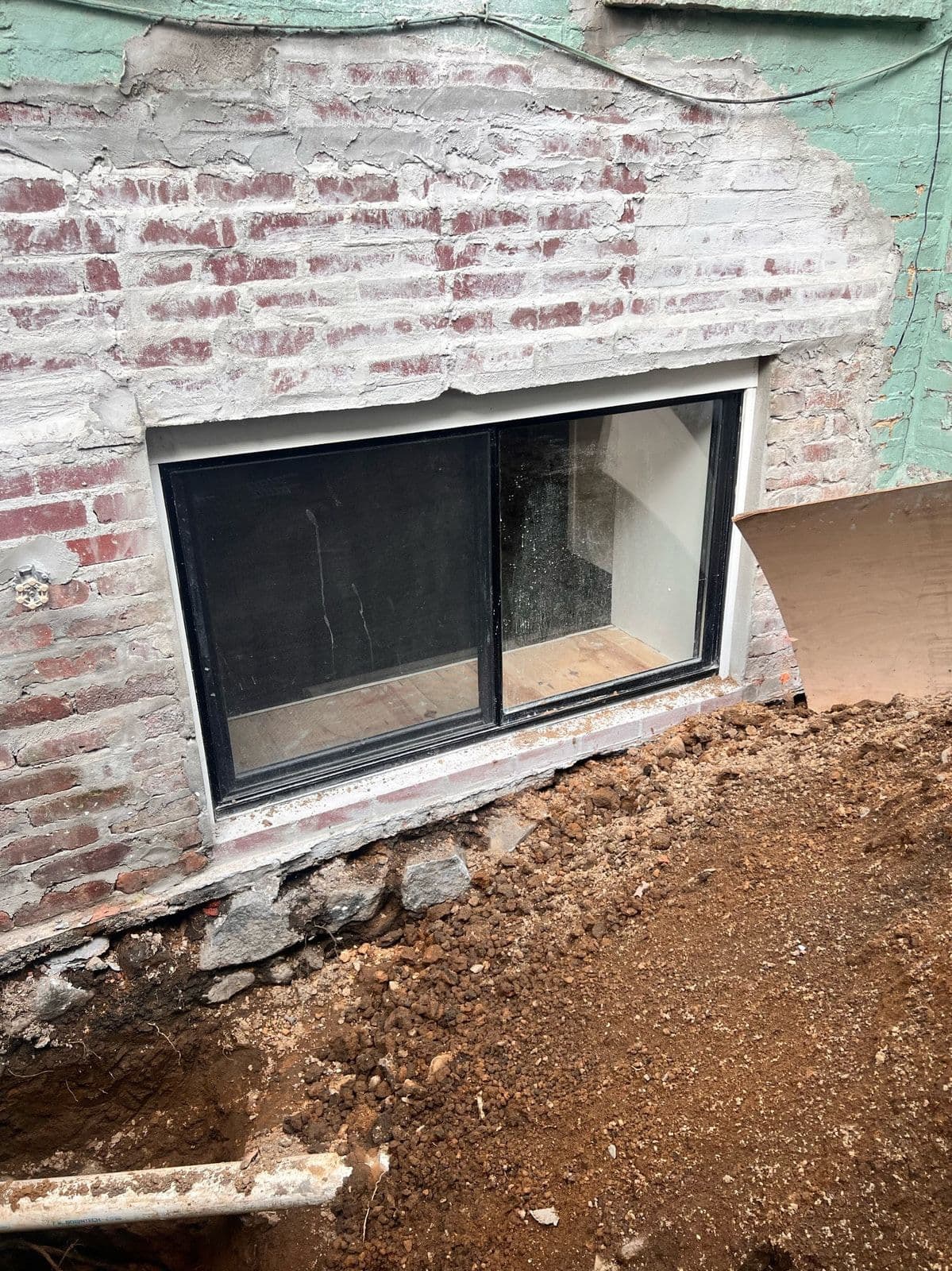 A new window set into the below-grade foundation wall, the trench in front of it still open.